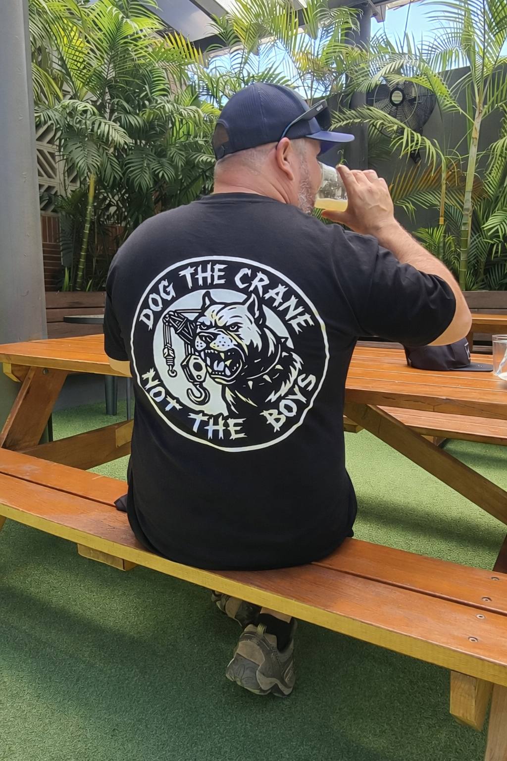 Man sitting at a picnic table wearing a black t-shirt with a graphic design and text.